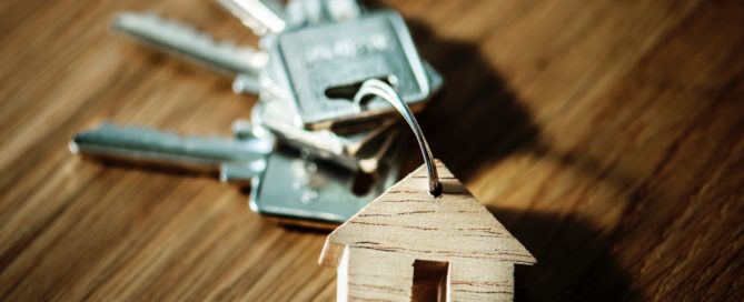 selective focus photography of four silver keys with brown house keychain on brown surface