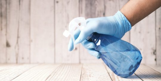 A hand in a blue latex glove holding a blue spray bottle